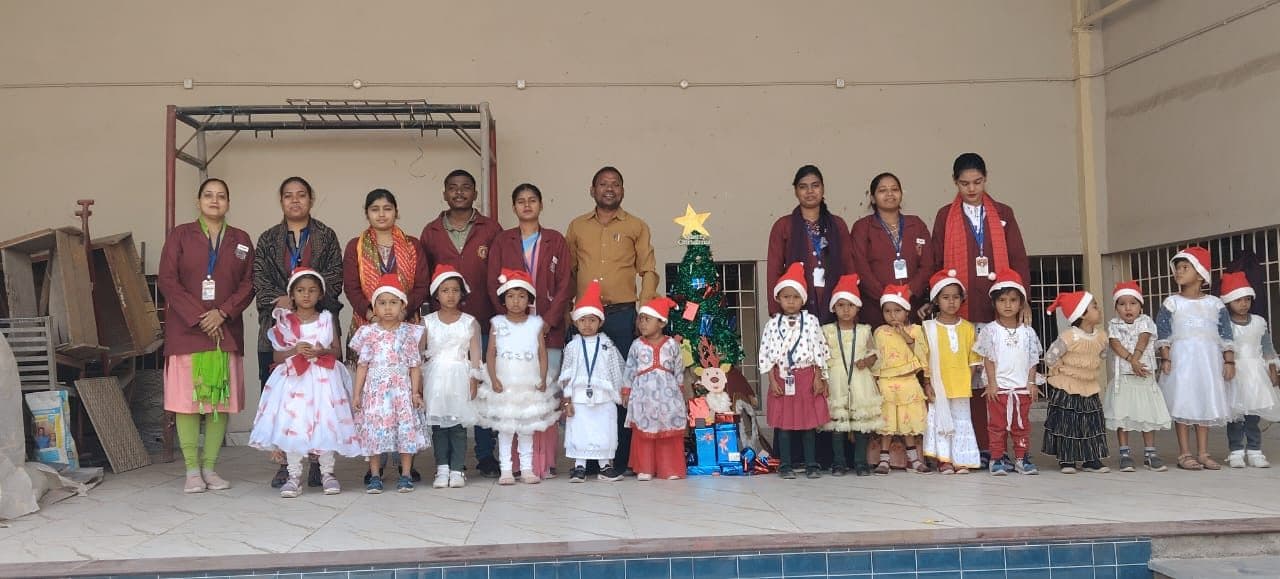 Pre-primary children in Santa hats beside a Christmas tree with their teachers